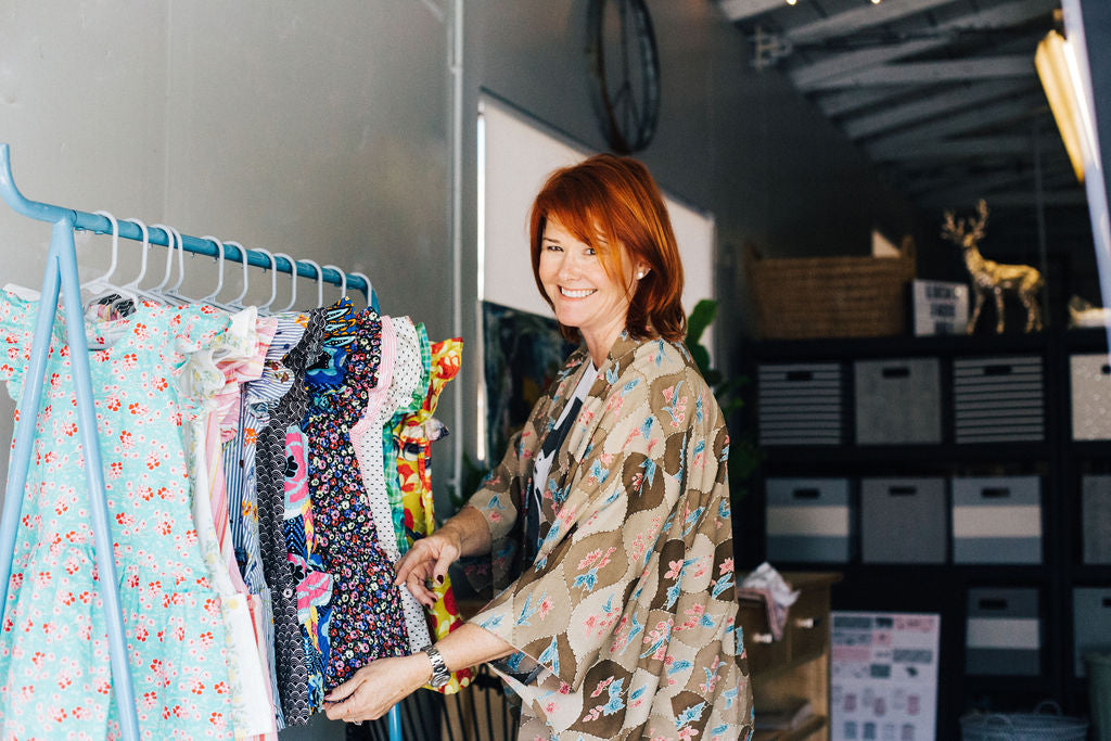 The founder of the company next to a rack of dresses  in the design studio   